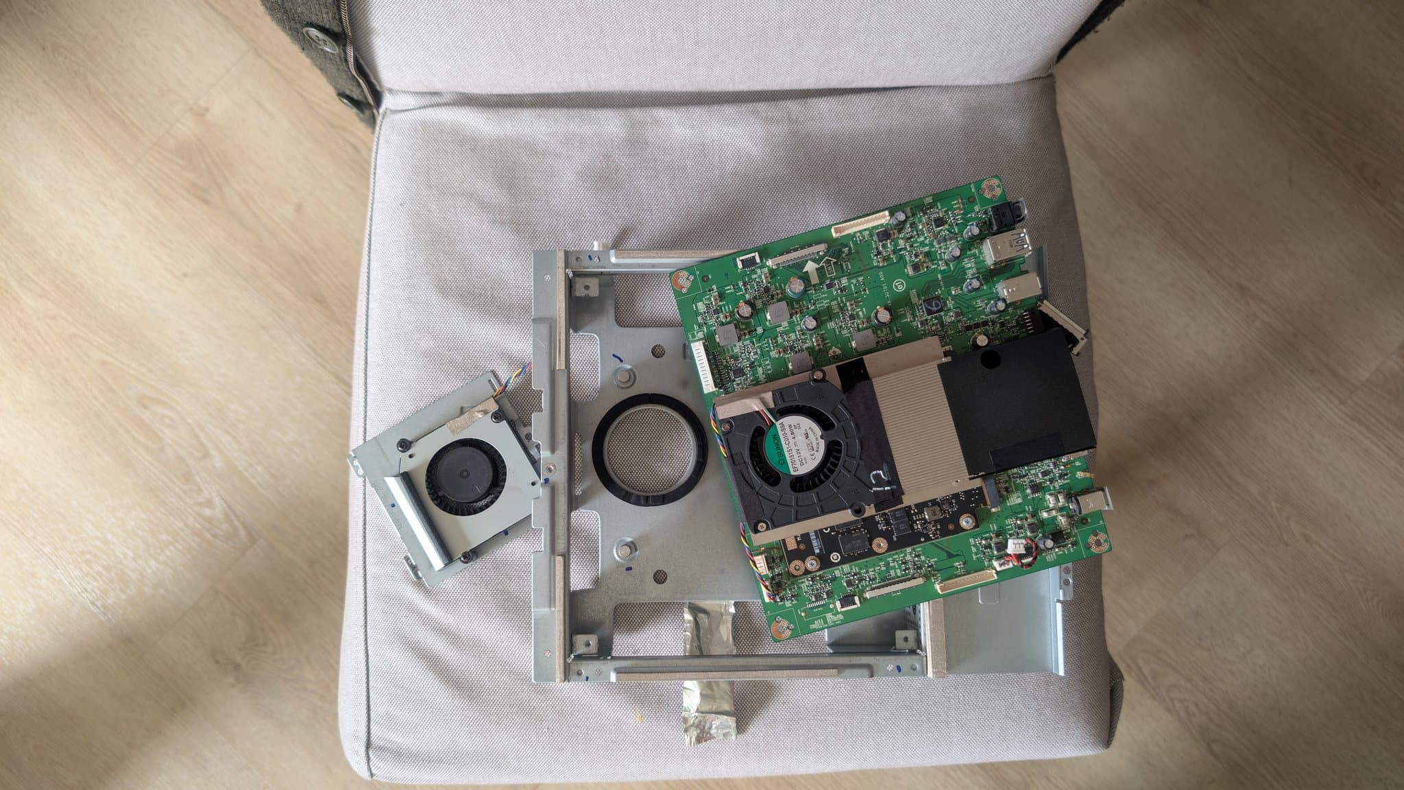 Disassembled Asus PG27UQ monitor internals showing dusty cooling fans, green PCB boards, and thermal paste residue on heatsink during refurbishment.
