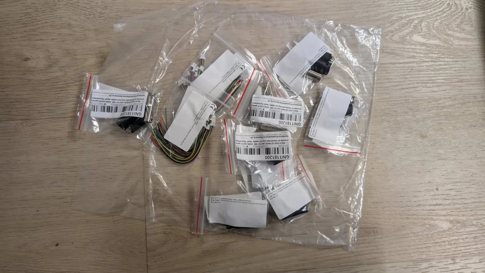Clear bags of WavePhoenix wiring parts on a wood surface with barcode labels: GameCube controller plugs, white JST connectors, and a bundle of multicoloured wire.