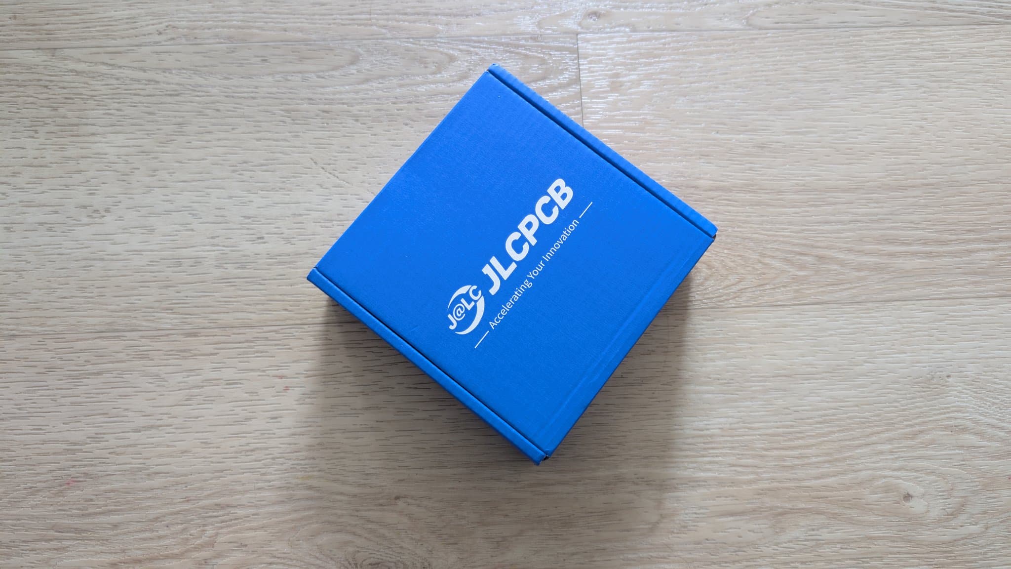 Blue JLCPCB box on wooden surface, containing pre-assembled WavePhoenix receiver PCBs for GameCube WaveBird controller modification.