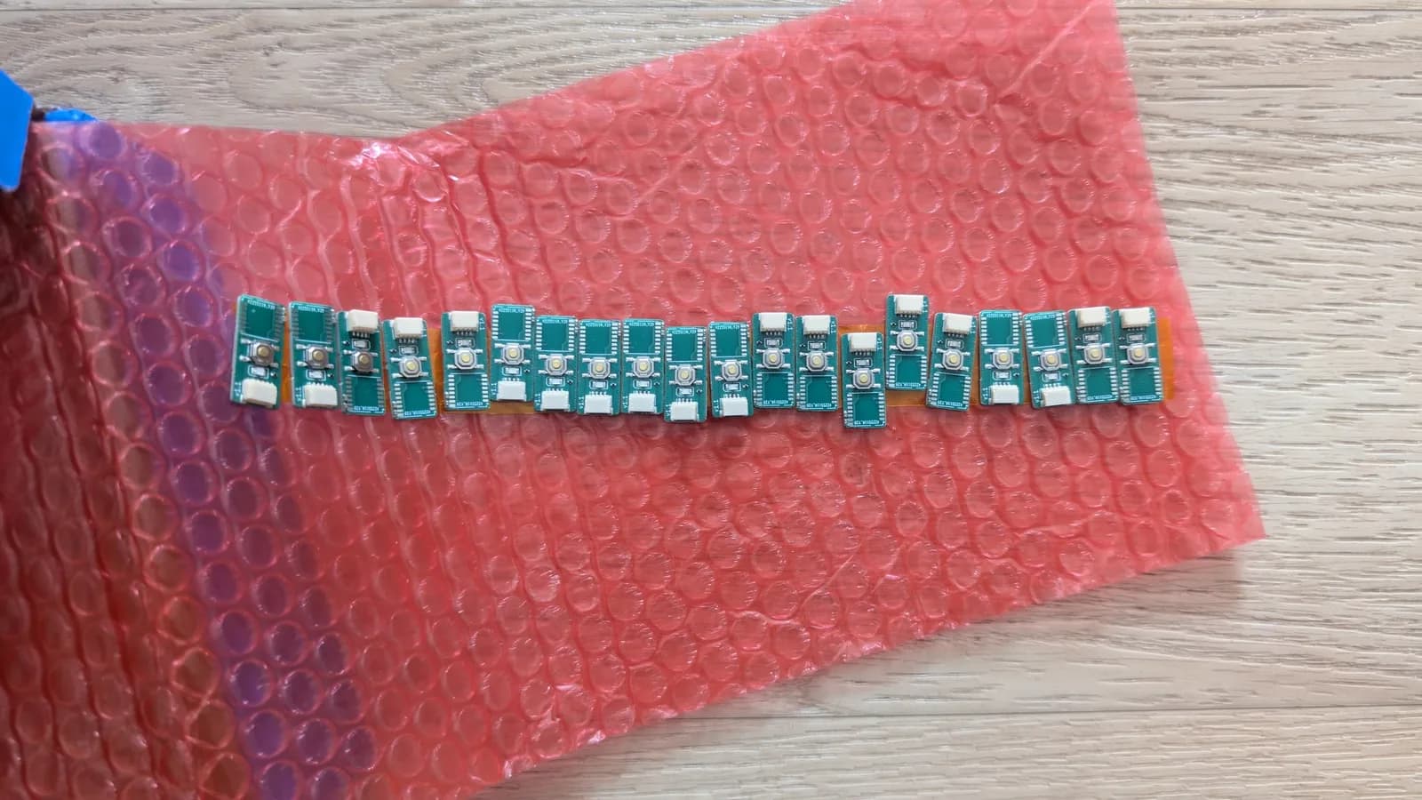 Row of green WavePhoenix receiver boards on red anti-static bubble wrap, each with a white JST connector and pairing button; pre-assembled by JLCPCB but still missing the radio module that powers the wireless link, which then has to be programmed.