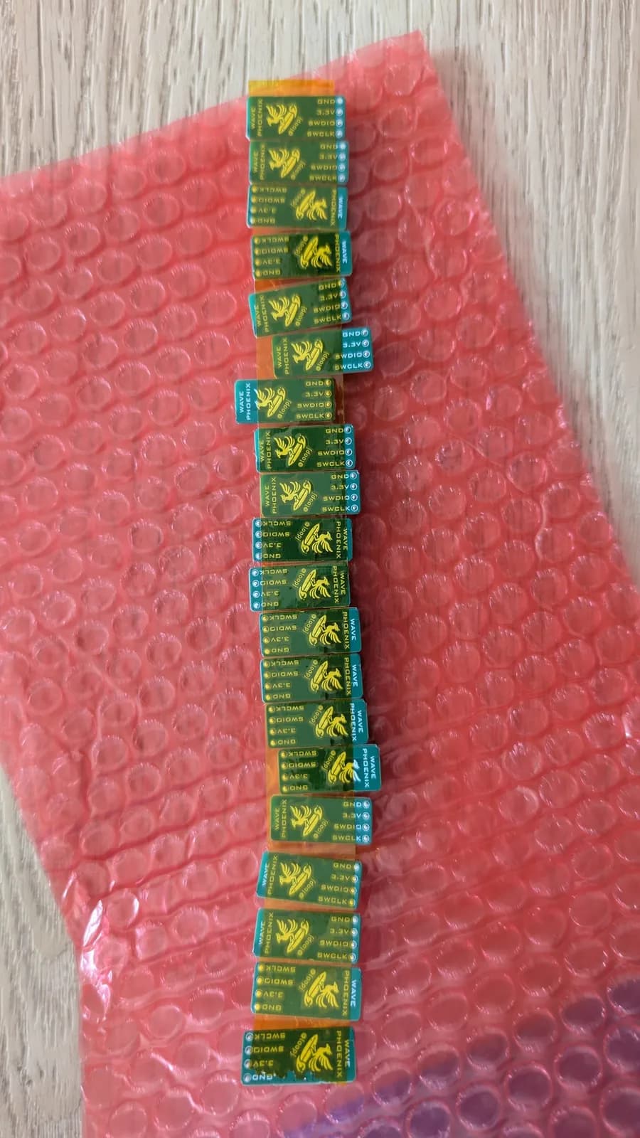 Green WavePhoenix receiver boards bound together with yellow Kapton tape and overlapping on red anti-static bubble wrap; their white silkscreen phoenix logos and 'loopj' marking look yellow through the tape.