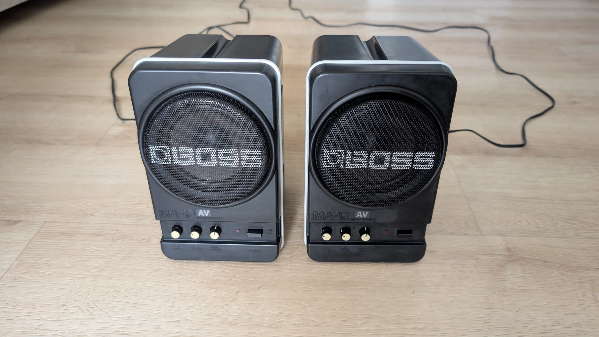 Pair of refurbished BOSS MA-12AV speakers after cleaning, showing restored black casings with visible speaker grilles and control knobs.