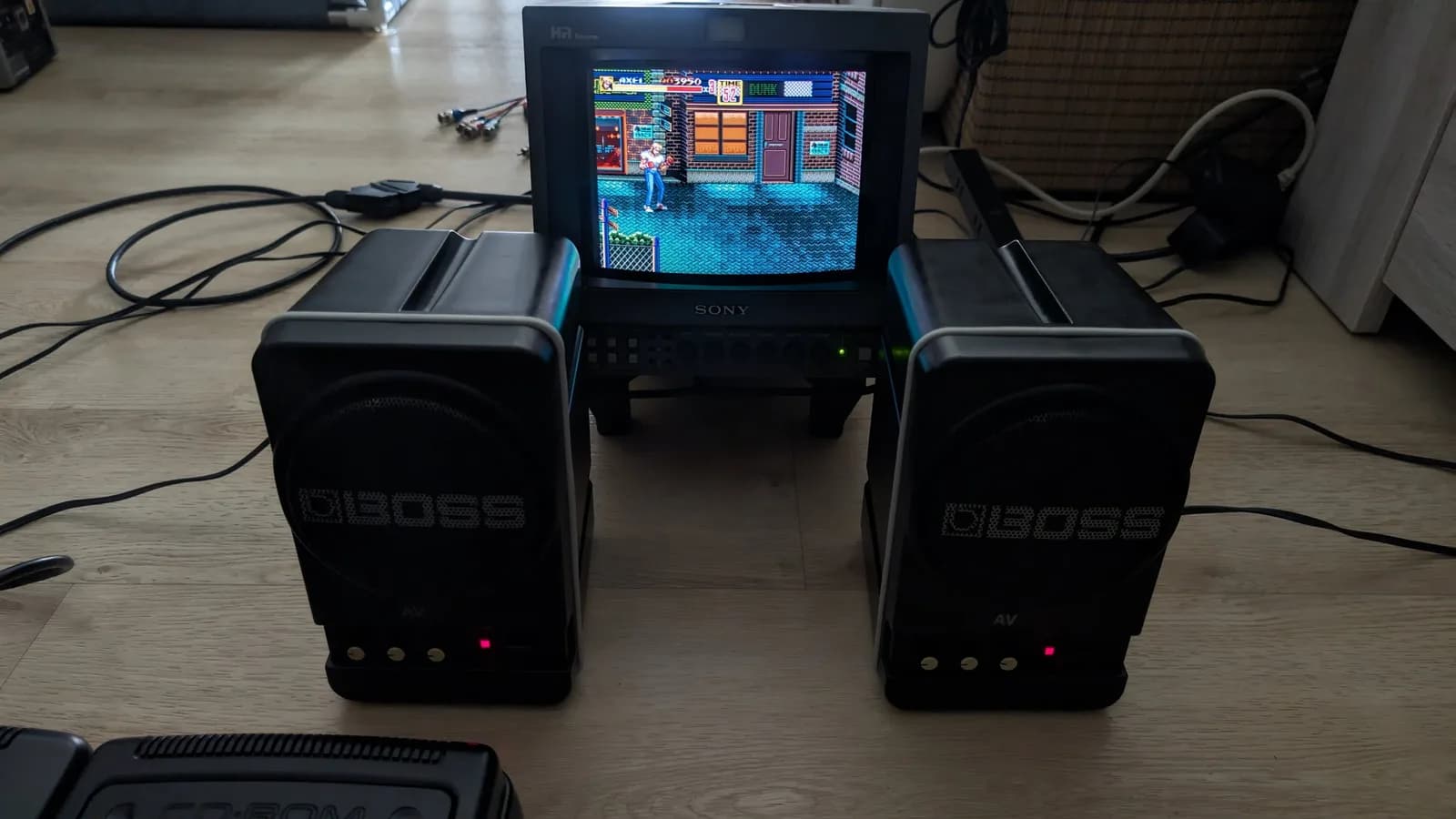 Pair of refurbished BOSS MA-12AV speakers flanking a Sony PVM-9045Q monitor displaying Streets of Rage gameplay, the red power LED on each speaker lit.
