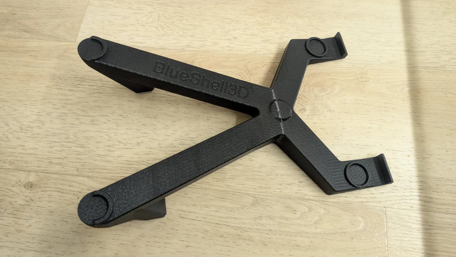 A black 3D-printed monitor stand embossed 'BlueShell3D' (for the 9-inch Sony PVM), with two arms at the front and two at the back that cross over near the back end, on a wood floor.