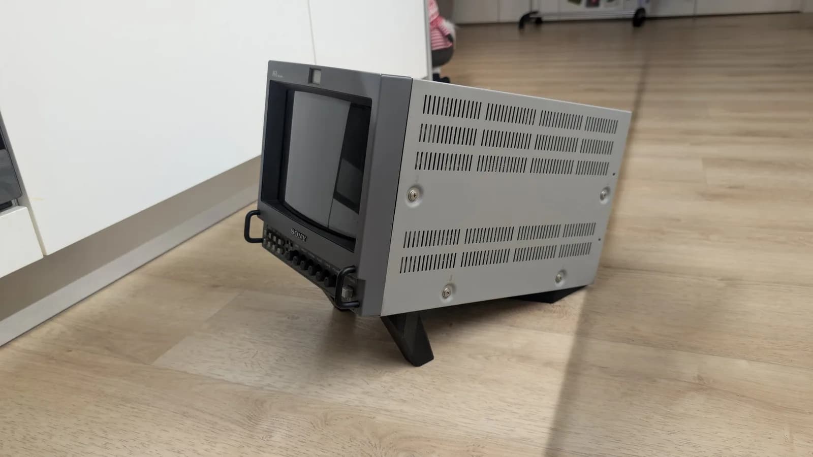 The restored Sony PVM-9045QD (screen off) tilted back on the black BlueShell3D 3D-printed stand, front three-quarter view on a wood floor.
