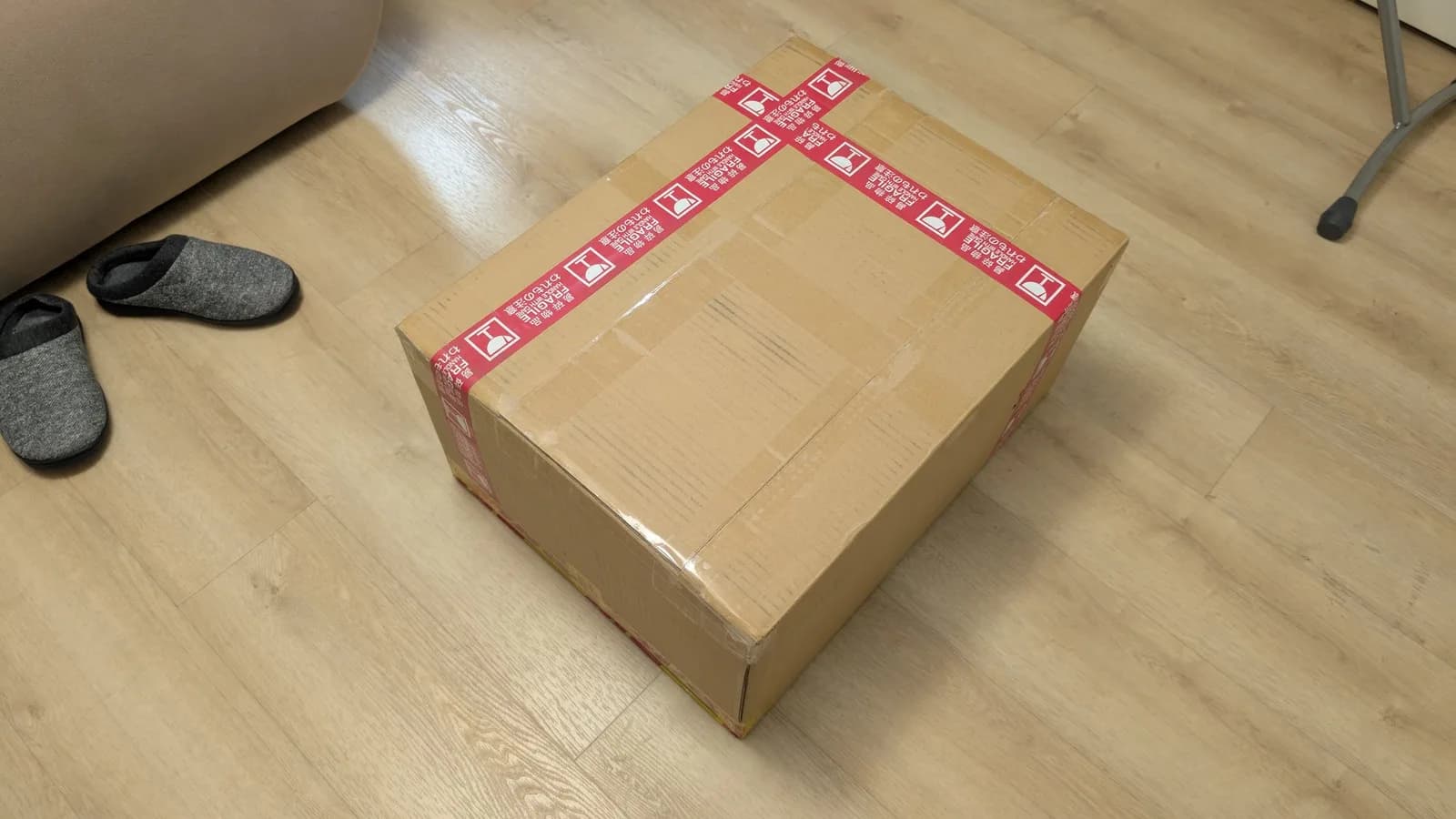 Sealed cardboard box with red packing tape on wooden floor, unopened Victor stereo unit shipped from Japan.