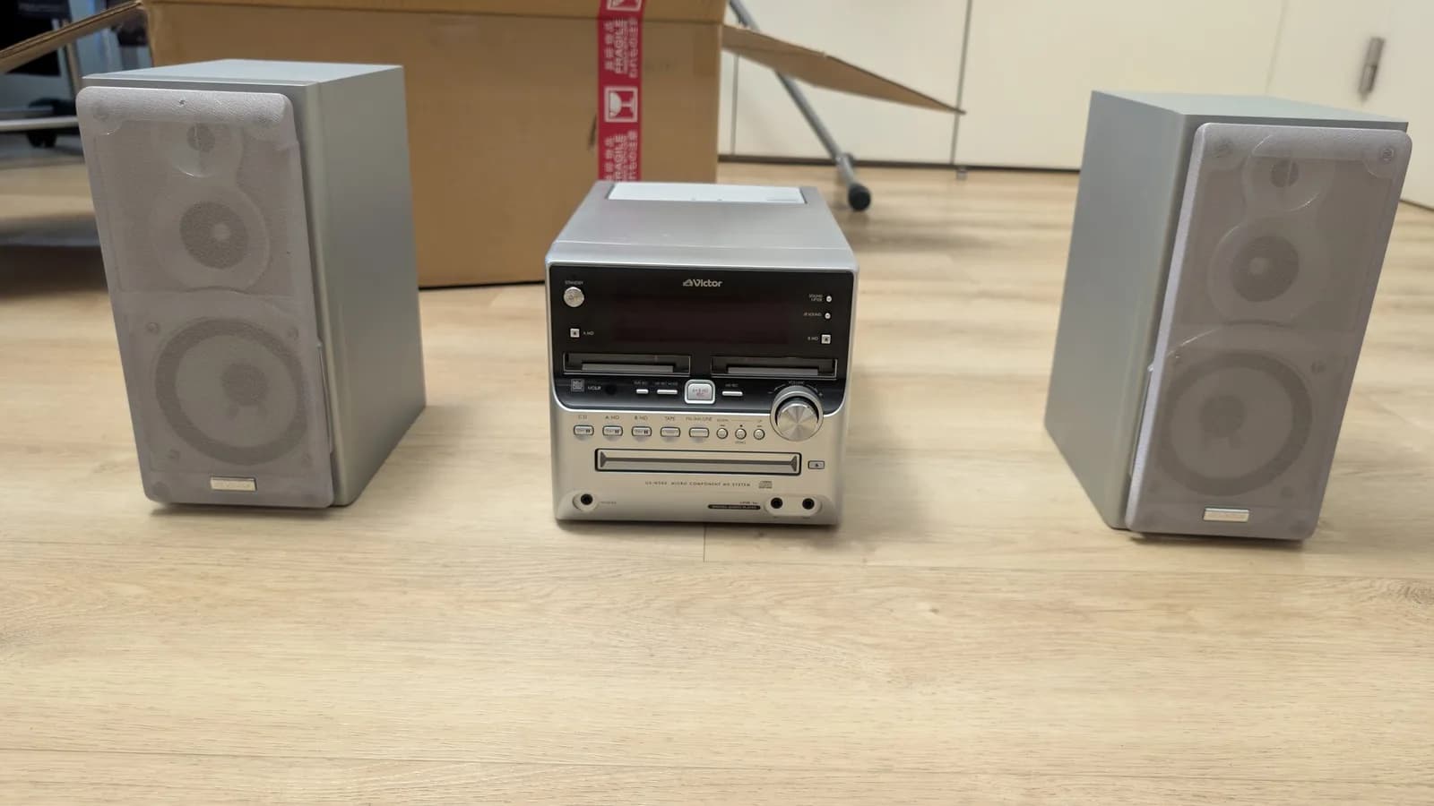 Victor stereo system with dual speakers and MiniDisc/cassette/CD player on wooden surface, cardboard box visible behind.