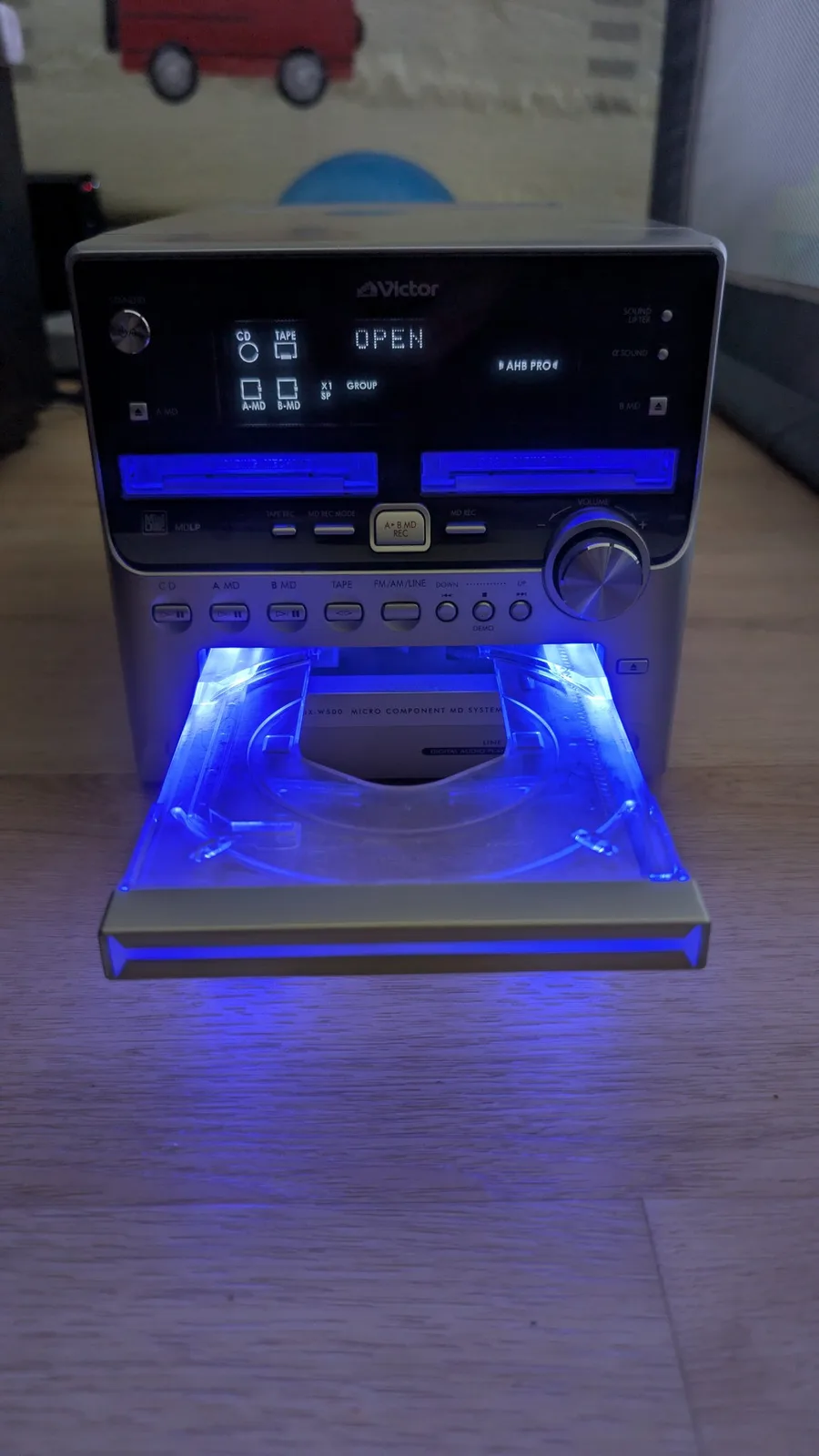 Victor stereo system with open disc tray illuminated by blue LED, displaying disc mechanism and loading components during MiniDisc repair work.