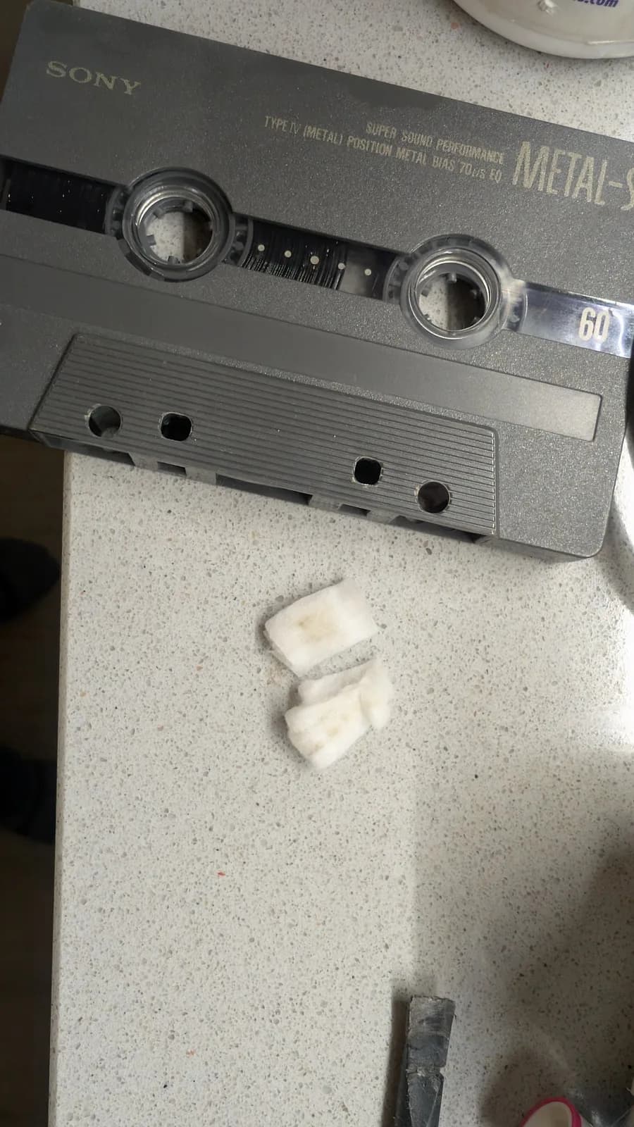 Sony metal cassette tape with two white cleaning blocks beside it; tape reels visible through windows.