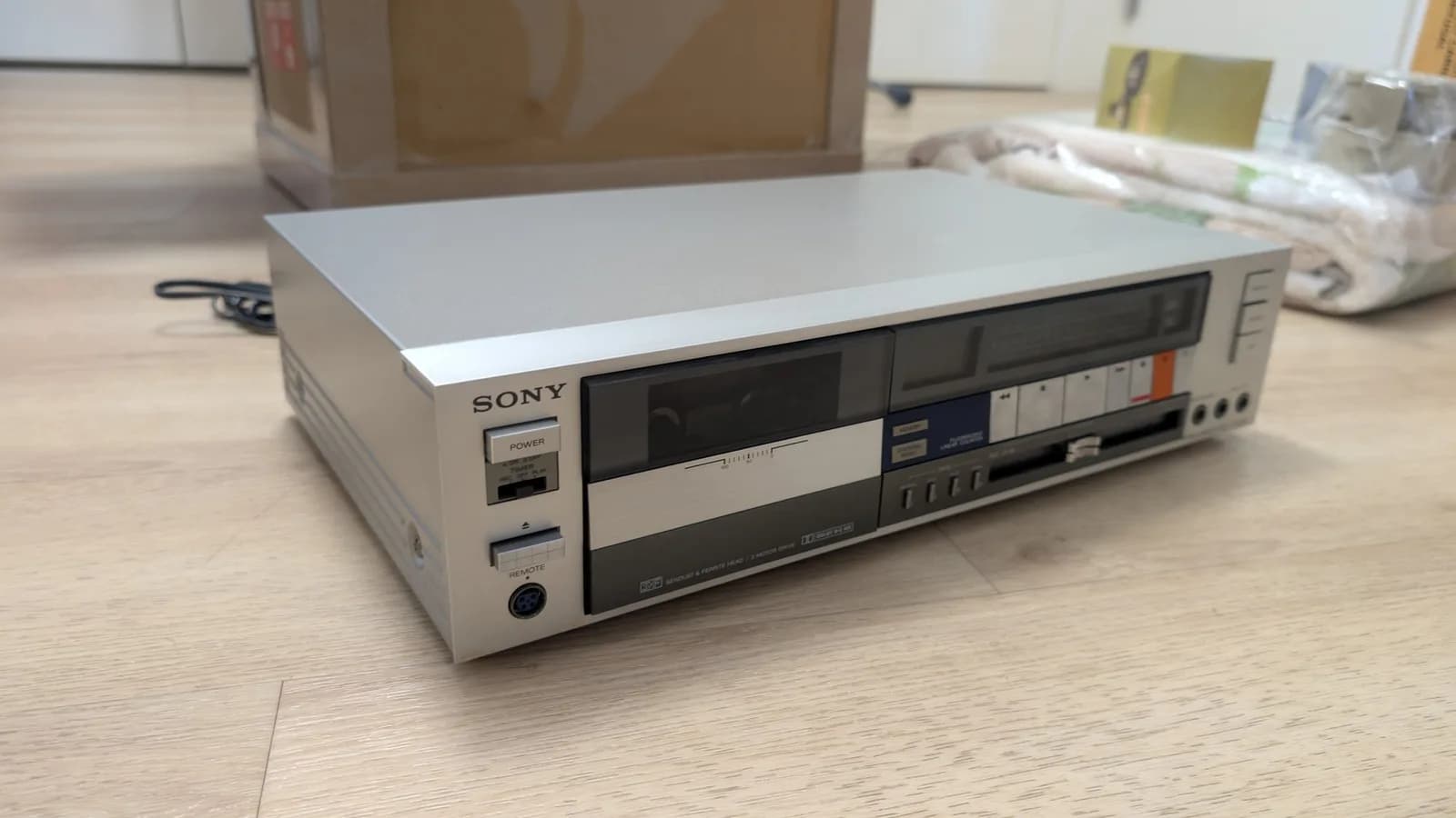Sony TC-FX66 tape deck exterior, cream and black casing, positioned on wooden floor showing front panel with dual cassette mechanisms and control interface.