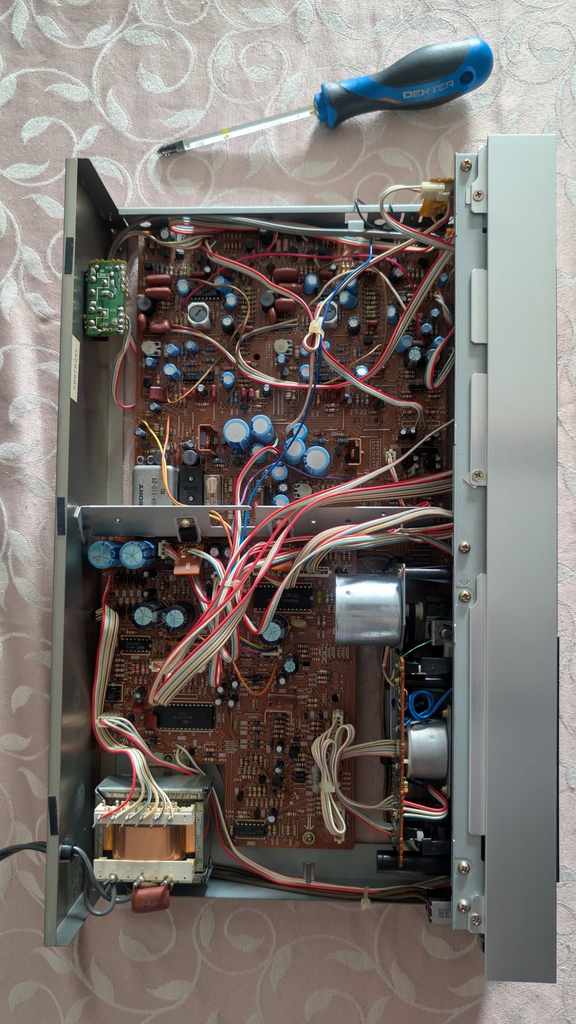 Interior of Sony TC-FX66 tape deck showing circuit boards, capacitors, transformers, and wiring with screwdriver positioned for repair work.