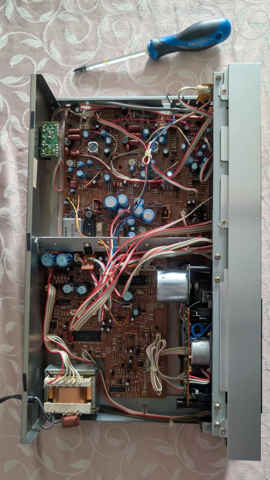 Interior of Sony TC-FX66 tape deck showing circuit boards, capacitors, transformers, and wiring with screwdriver positioned for repair work.