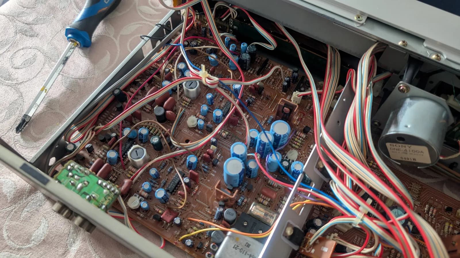Interior of Sony TC-FX66 tape deck showing circuit boards with blue capacitors, red and blue wiring, and brown transformer, screwdriver visible for service work.