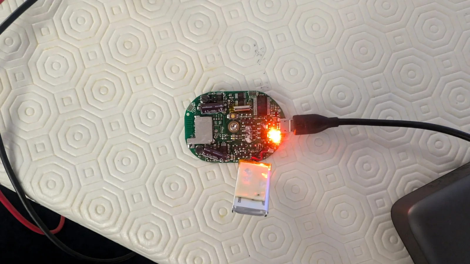 PowerDot circuit board with illuminated red LED, USB port connector below, soldering iron actively heating component during repair.