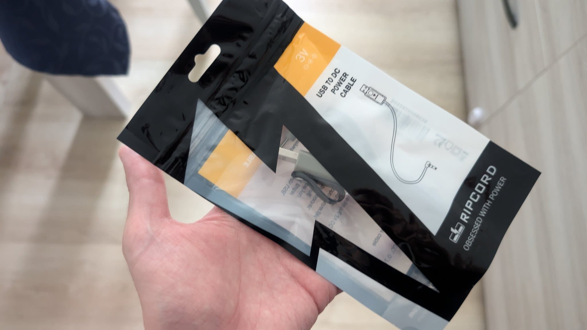 Hand holding MiniDisc charging cable package with USB power adapter and cord visible through clear packaging window.