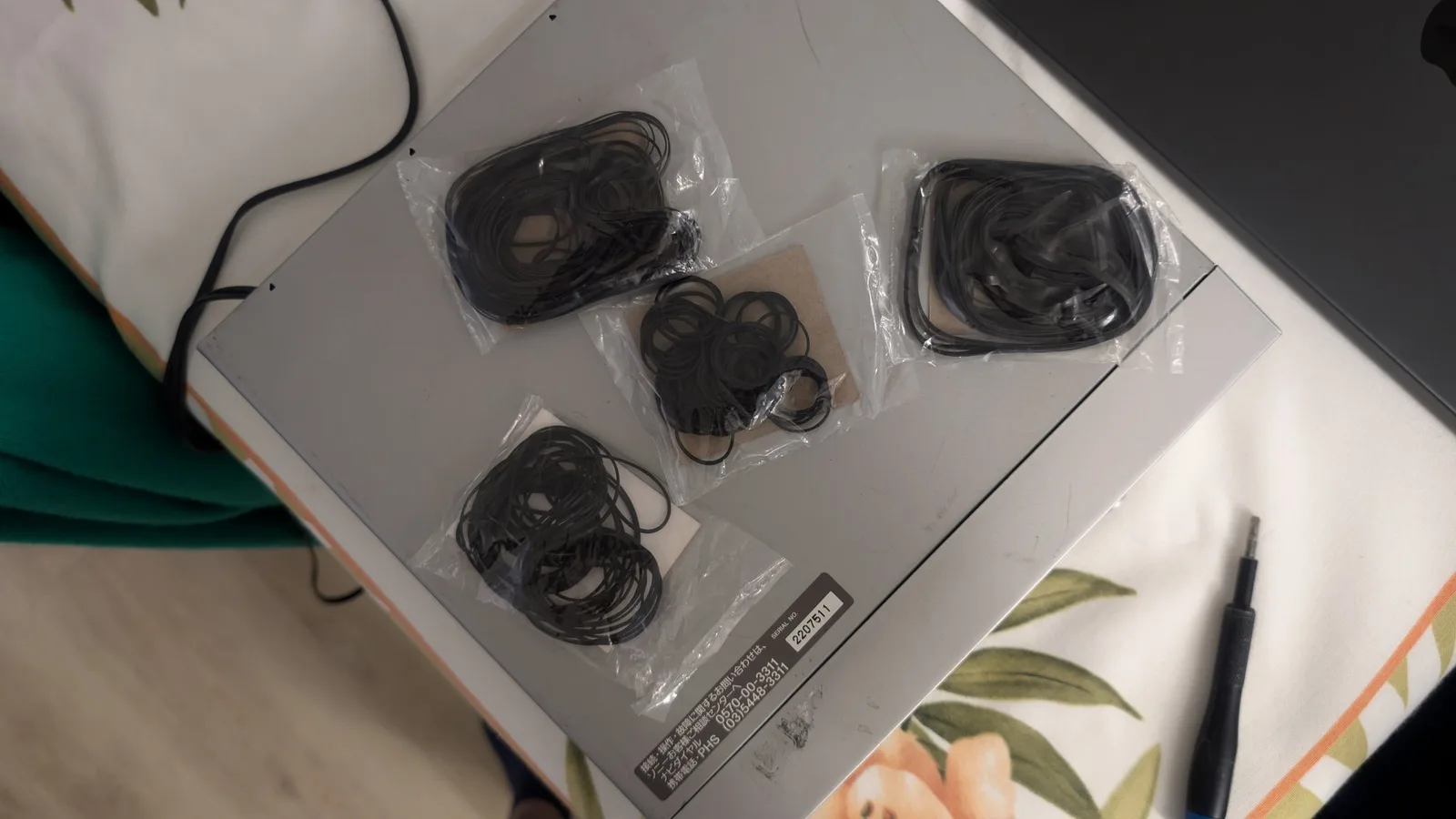 Four replacement belts in clear plastic packaging arranged on white surface with repair documentation and stylus nearby.