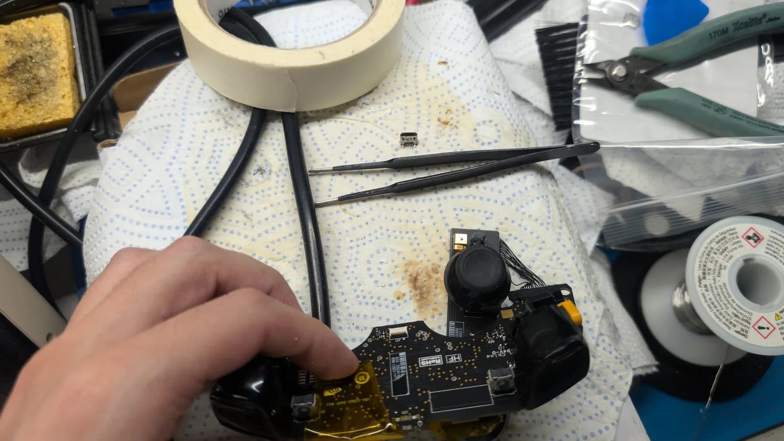 Technician's hand holding Nvidia Shield controller PCB with newly soldered USB port replacement during testing on workbench with tools nearby.