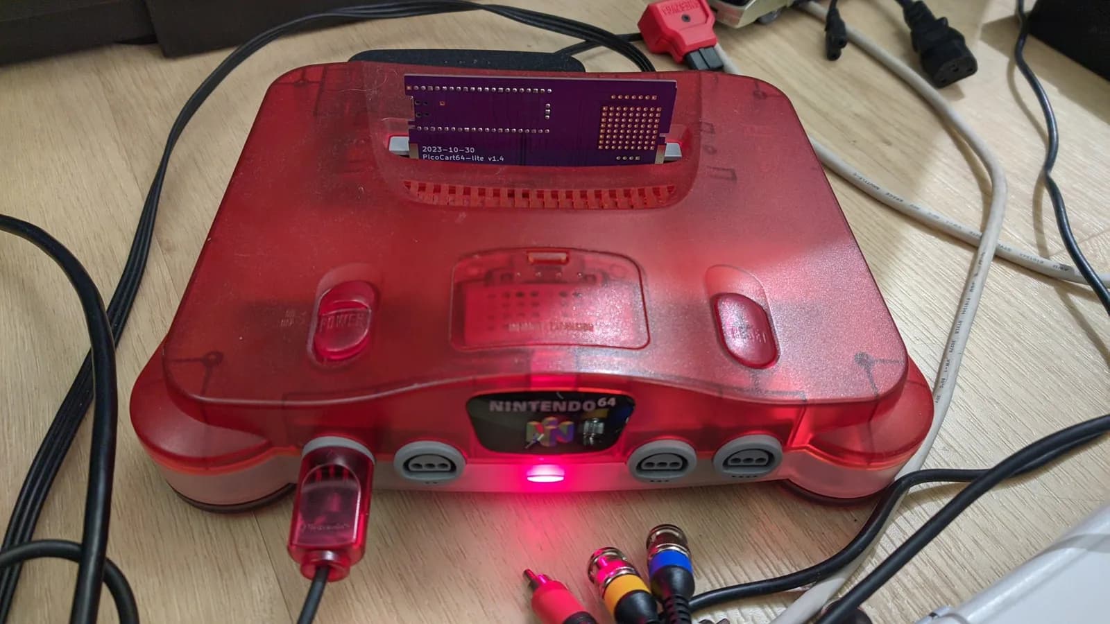 Red Nintendo 64 console with PicoCart-lite v1.4 board installed, LED indicator glowing, connected via composite cables.