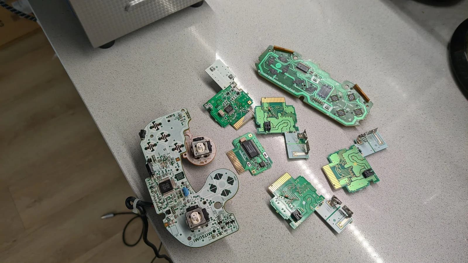 Disassembled Nintendo console PCBs and controller boards laid out after ultrasonic cleaning, showing green circuit boards with exposed solder joints and connectors.