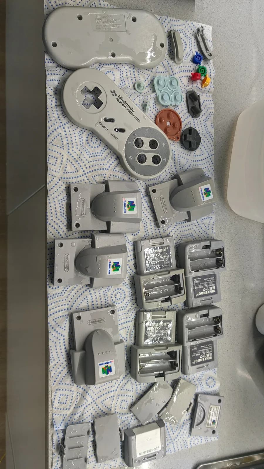 Disassembled Nintendo 64 controller parts and accessories laid out on dotted cloth after ultrasonic cleaning, including shells, circuit boards, and battery covers.