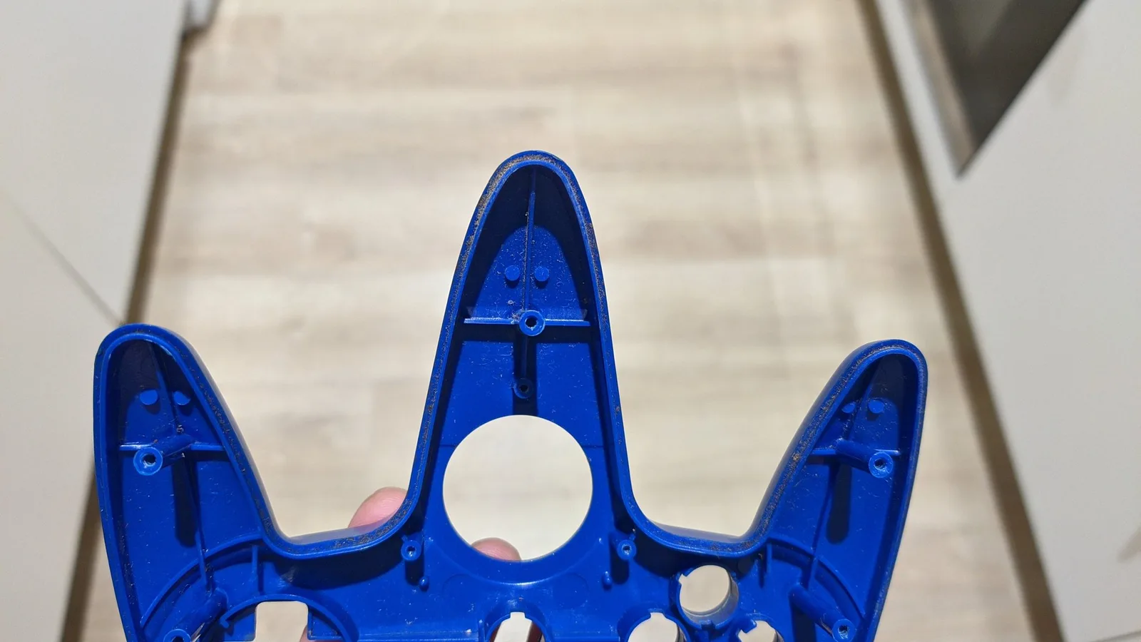 Blue controller shell in ultrasonic cleaner basket, showing internal detail and cross-shaped component holder, stairs visible in background.