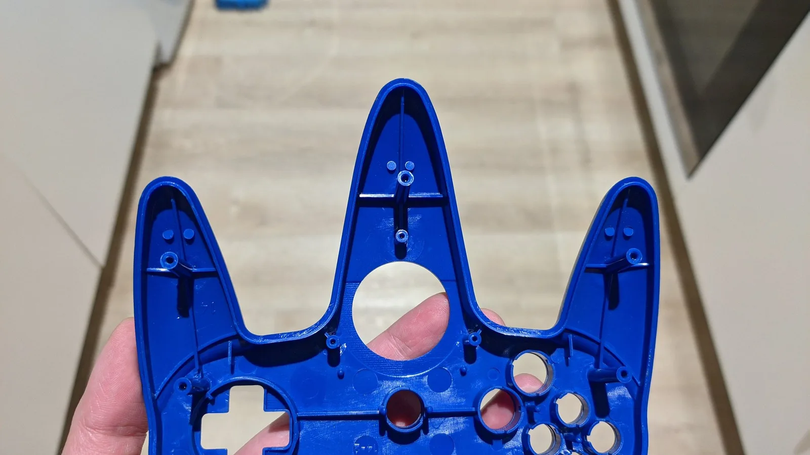 Bright blue controller shell held in hand, showing cleaned interior cavity with visible button mechanisms and mounting points after ultrasonic cleaning.