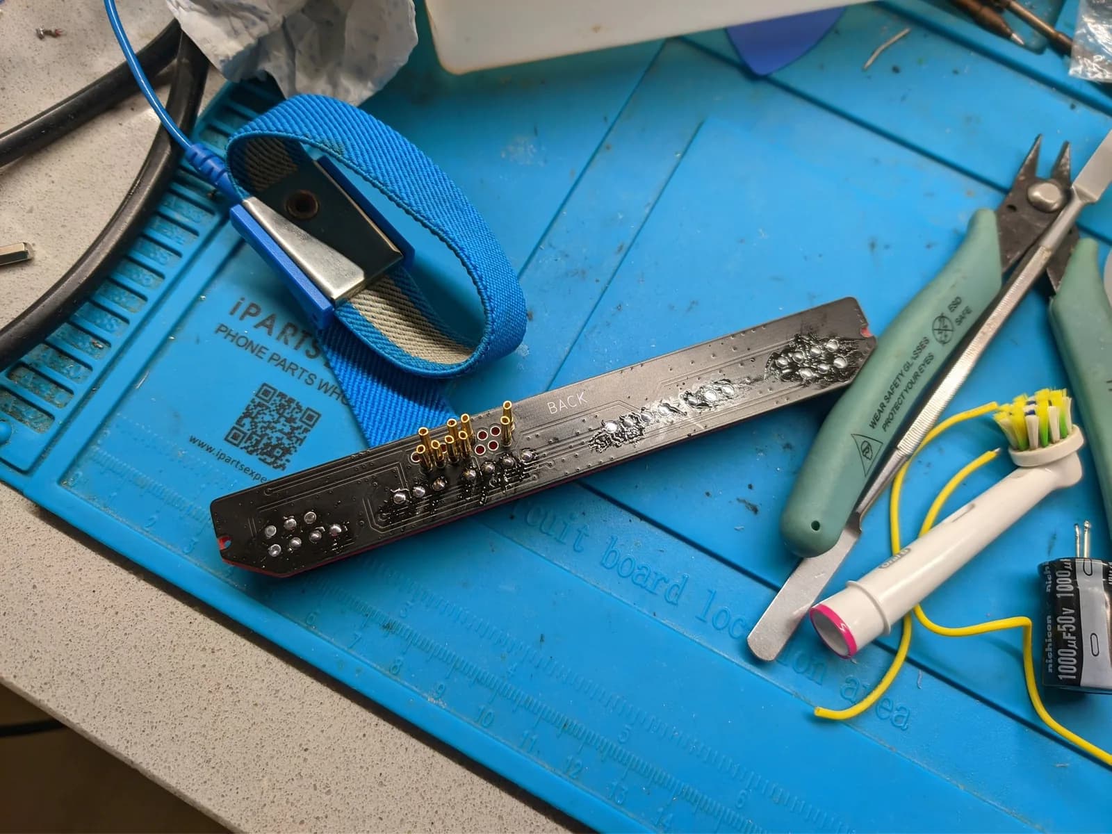 Famicoun NES controller adapter PCB with exposed solder joints, yellow wiring, and repair tools on blue work mat.