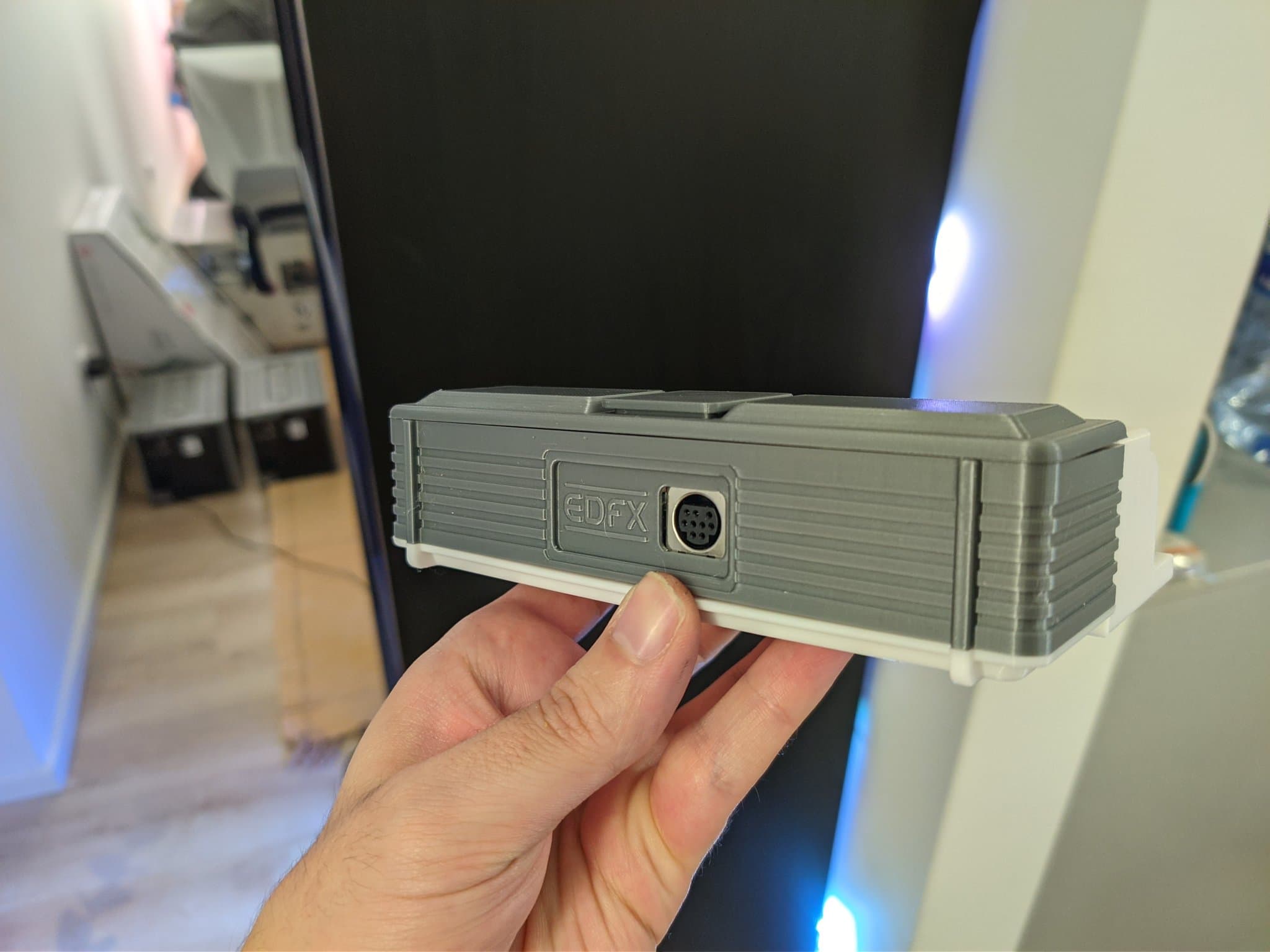 Hand holding the Krikzz EDFX in its 3D-printed mini-IFU shell. The EDFX is an adapter that plugs into the PC Engine Ext Bus port to pull out audio and RGB (or composite) video, not a cartridge; its recessed connector port and the shell's ribbed detail are visible.
