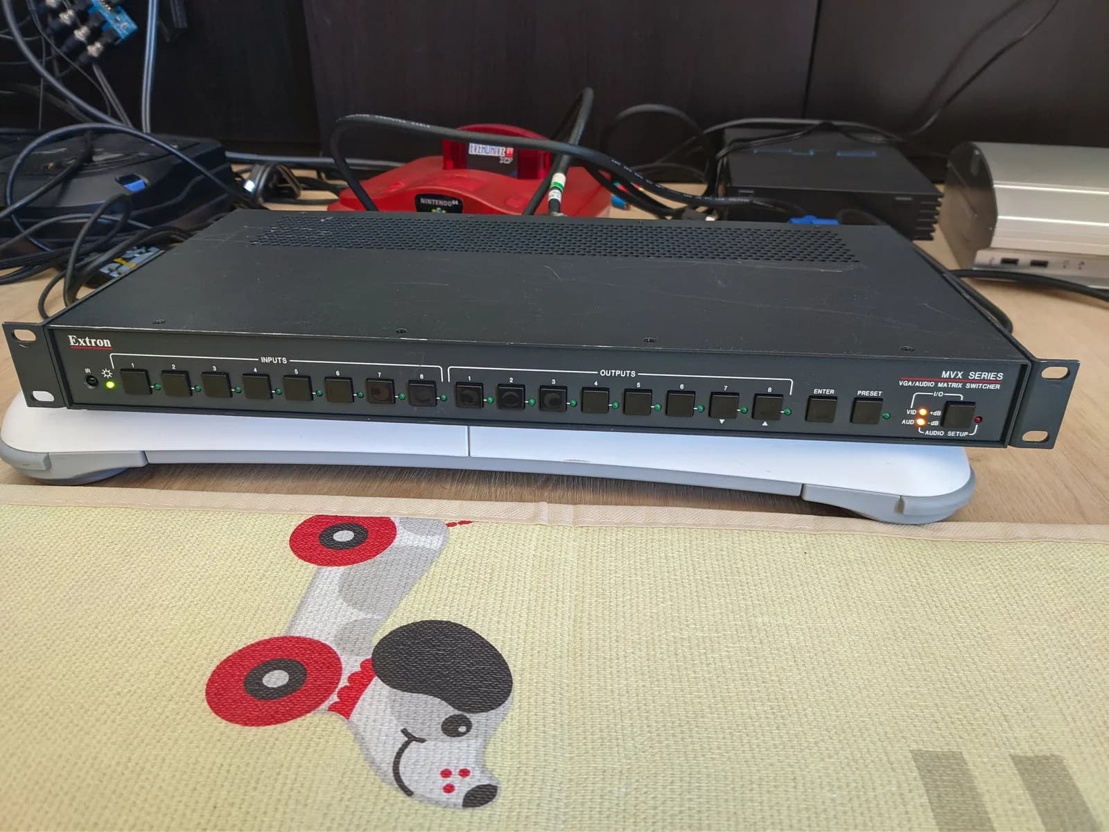 Extron MVX matrix switcher sitting on top of a white Wii Balance Board; also in shot are a PlayStation 2 fat, a Mega Drive 2 with Mega-CD 2 combo, and a silver Metal Gear Solid 4 edition PlayStation 3.
