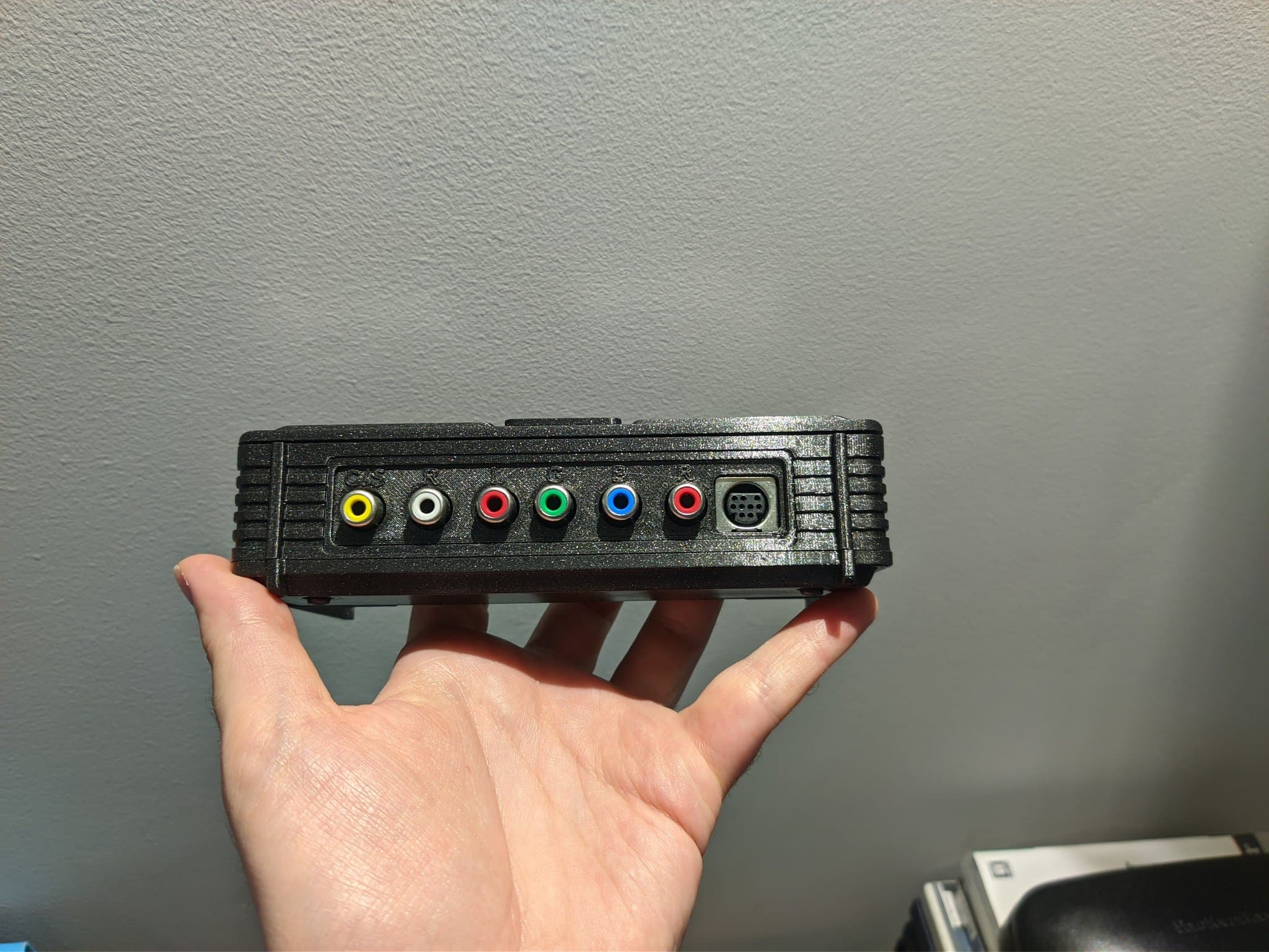 Hand holding the PC Engine AV adapter in a PointerFunction 3D-printed enclosure, showing its RCA connectors and a 9-pin mini-DIN port (the same type the EDFX uses, for a Mega Drive 2 RGB cable).