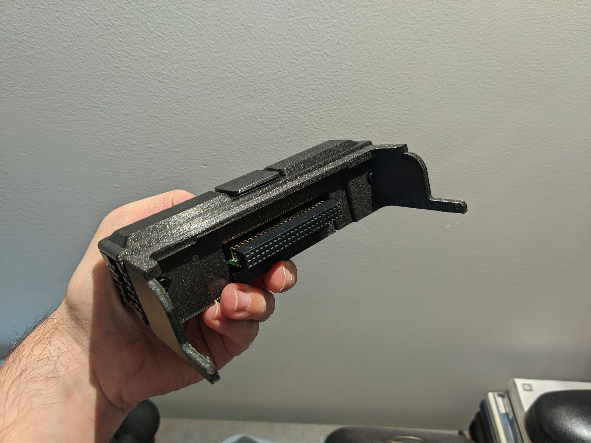 The PC Engine AV adapter in a PointerFunction 3D-printed enclosure, viewed from the side where the Ext Bus connector protrudes, with a perforated metal grounding plate and a green indicator light.