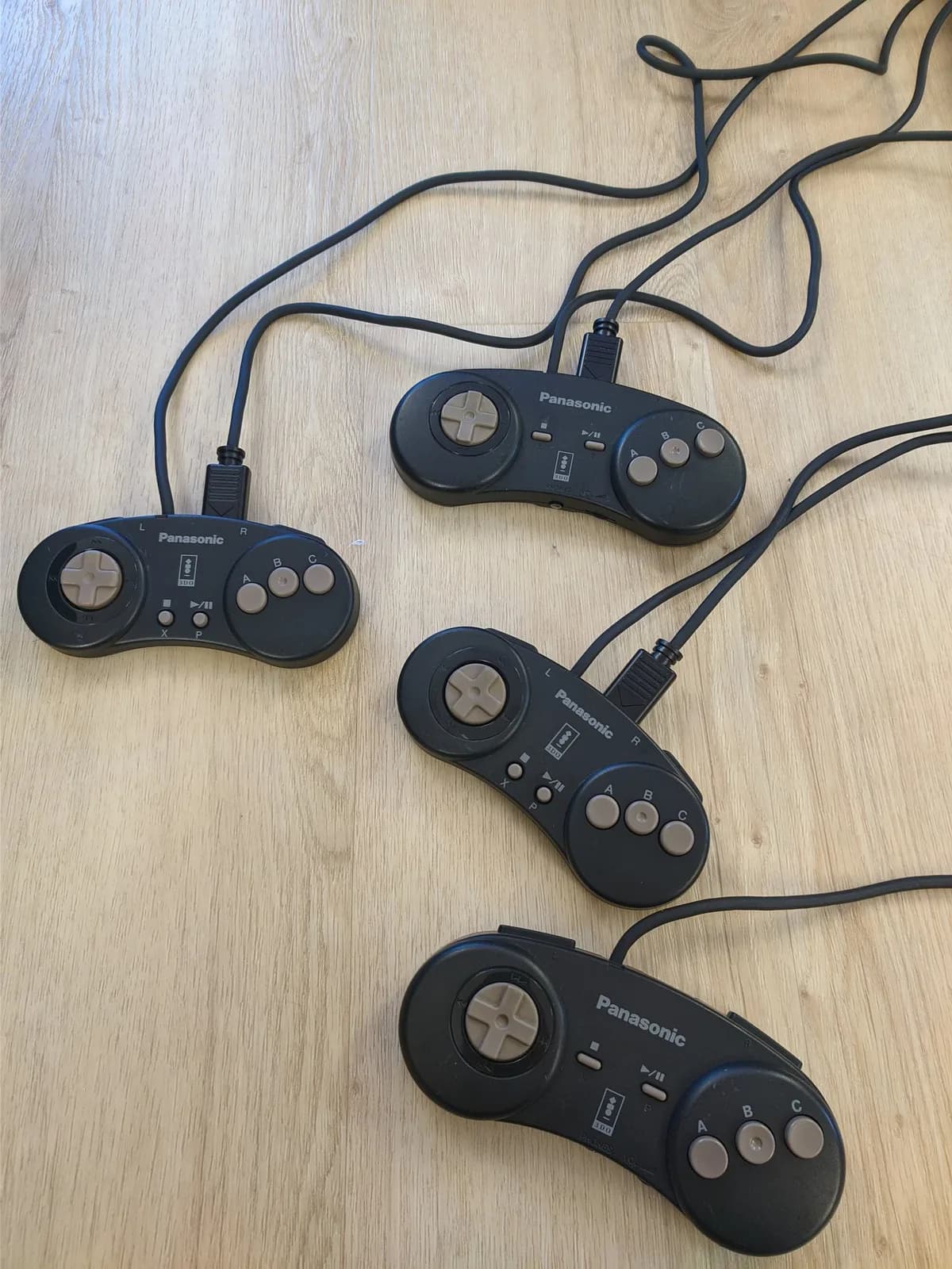 Four Panasonic 3DO controllers with cables on wooden surface, showing refurbished condition after capacitor replacement and cleaning.