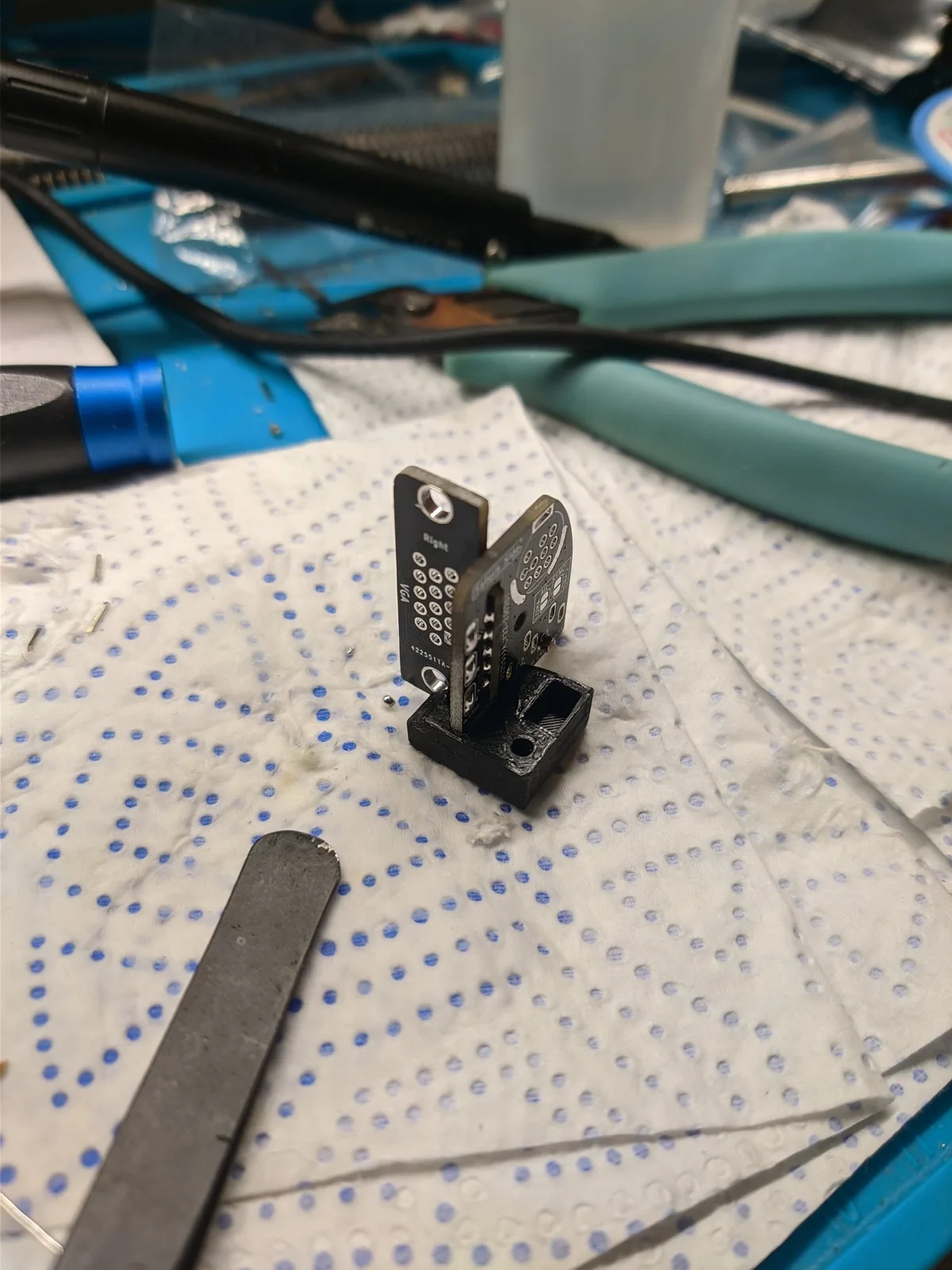 A partly assembled 10DIN2VGA (Saturn) dongle on a paper towel over a blue work mat, with a soldering iron and hand tools nearby.