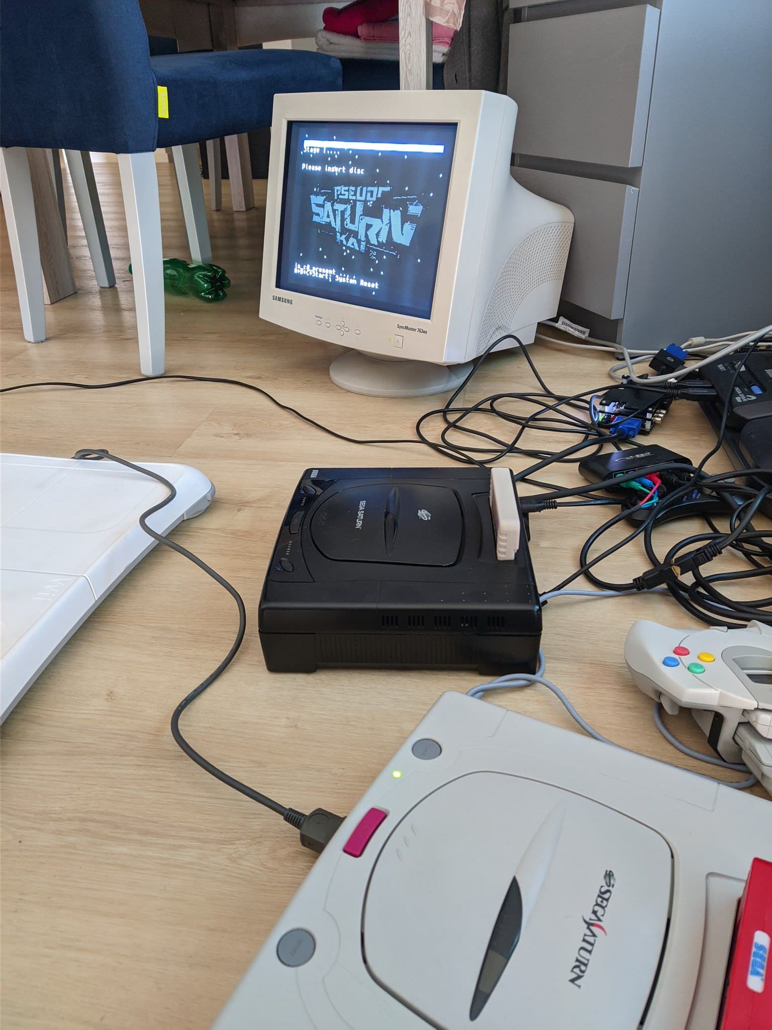 Two Jeff Chen 10DIN2VGA dongles for Sega Saturn displayed—PAL black model and NTSC white model—connected to vintage gaming setup with controllers and CRT monitor.