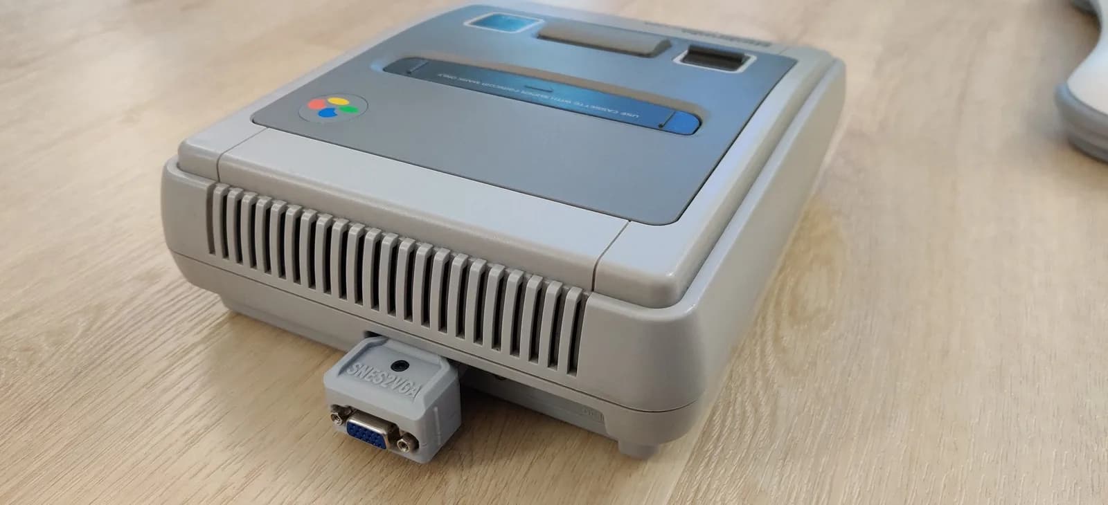 André's PAL 1-CHIP Super Nintendo on a wooden surface, with the grey-shelled SNES2VGA dongle (the PAL-configured build) plugged into its multi-out.