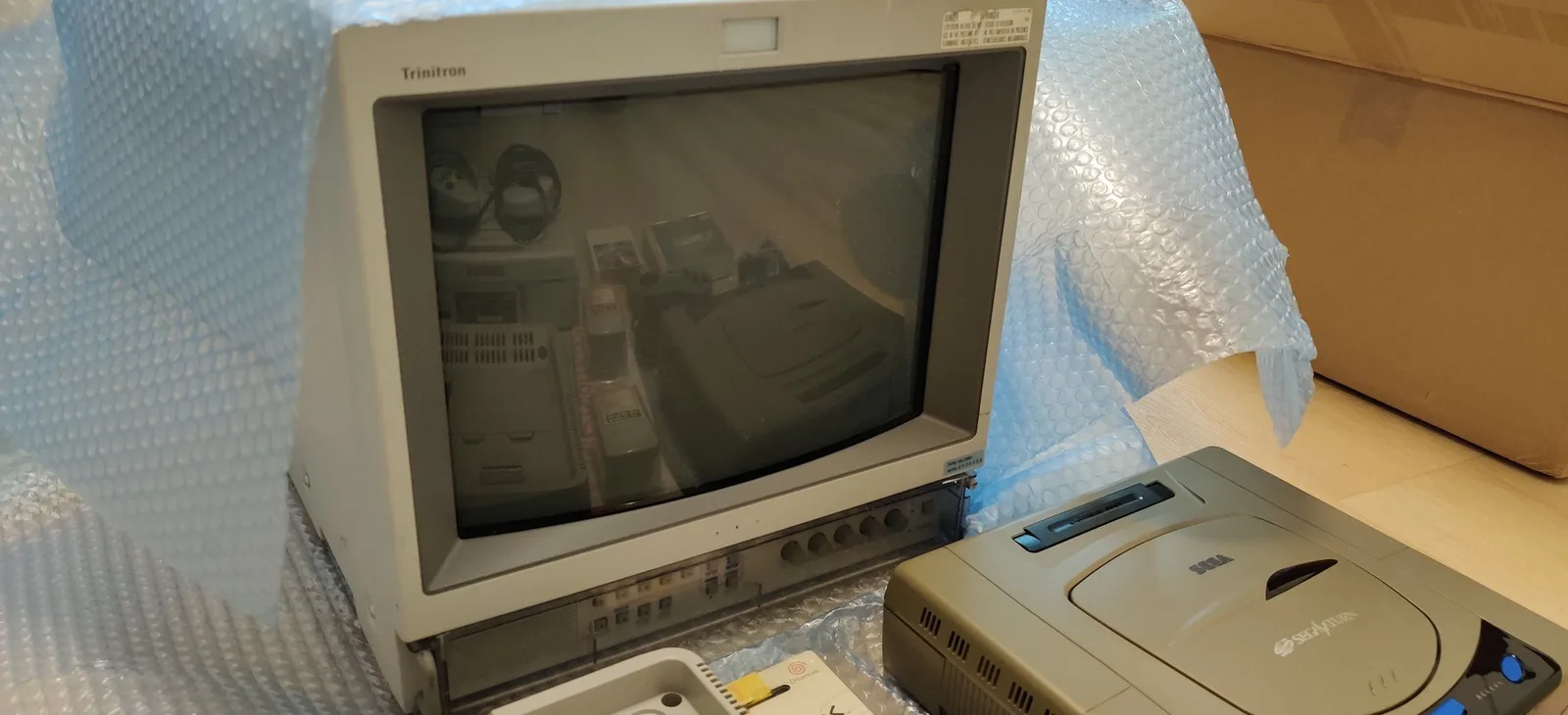 Trinton CRT monitor displaying composite video from Sega Saturn and other retro gaming hardware on wooden desk with bubble wrap.