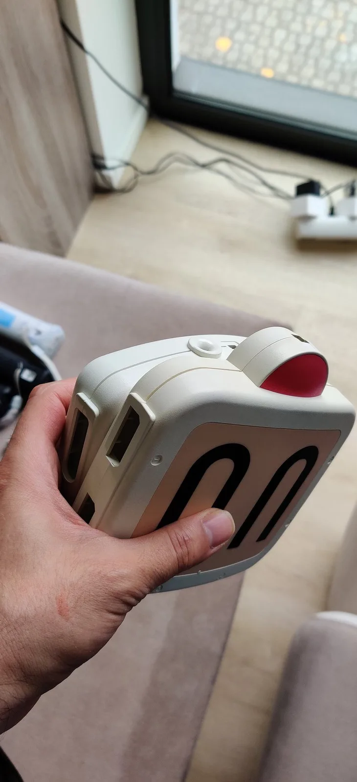 Hand holding white Sega Master System controller with red thumb pad, showing retrobriting results on desk.
