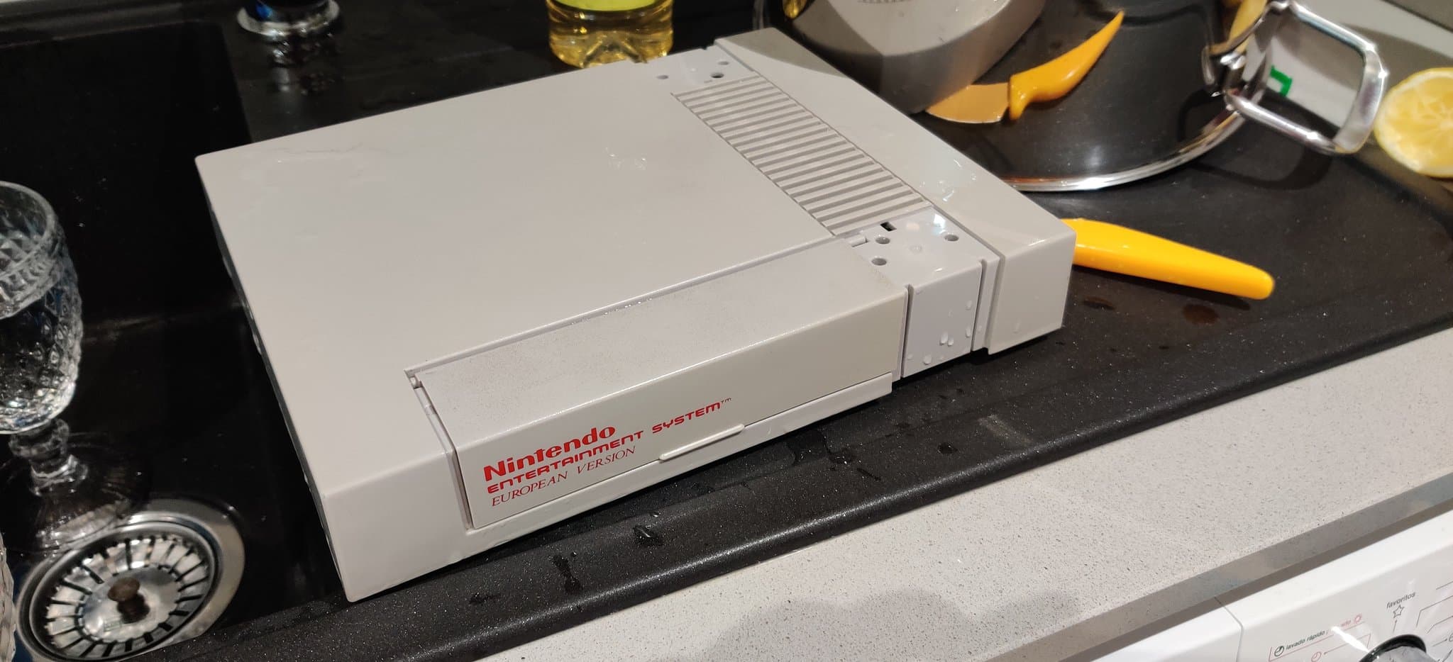 Nintendo Entertainment System European version on black desk surface surrounded by retrobriting supplies and tools.