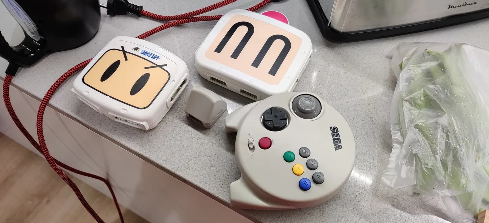 Retrobriting batch: two white gaming controllers with character faces, heating pad with dual coils, and white game controller with colored buttons on work surface.