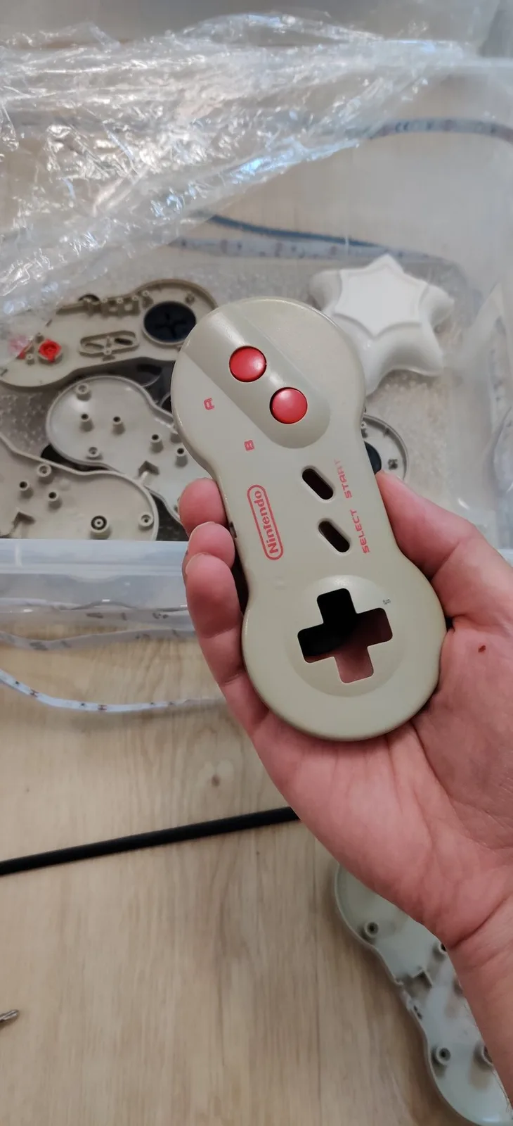 White Sega controller during retrobriting, showing disassembled shell parts and red button caps in background.