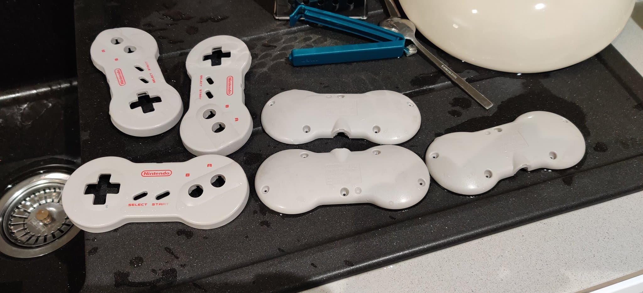 White Nintendo controllers in various stages of retrobrighting on black surface, showing yellowing reversal treatment.