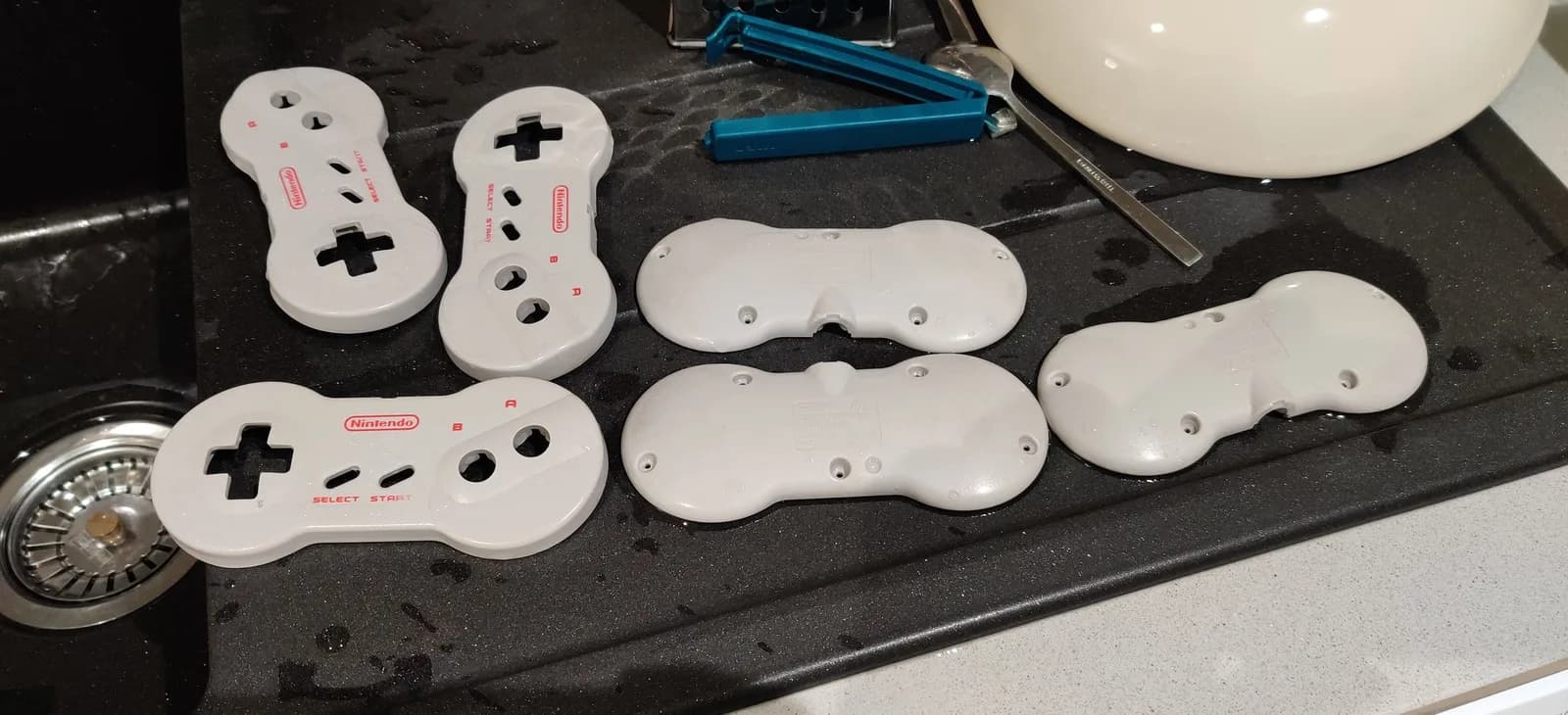 White Nintendo controllers in various stages of retrobriting on black surface, showing yellowing reversal treatment.