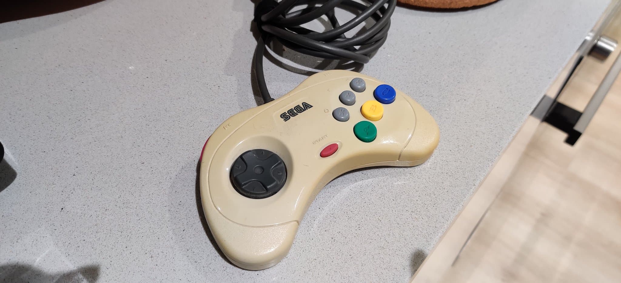 Cream-colored Sega controller with colored buttons on light surface, showing retrobrighting results from SG-1000 II recap repair.