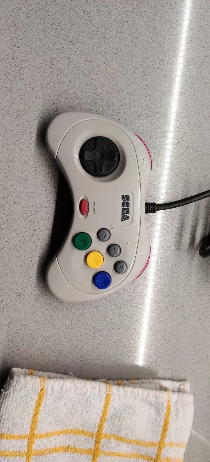 White Sega controller with colored face buttons (red, green, yellow, blue) on concrete surface during retrobriting restoration session.