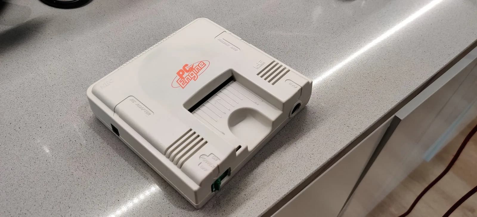 White PC Engine console with red logo undergoing retrobriting treatment, displayed on work surface.