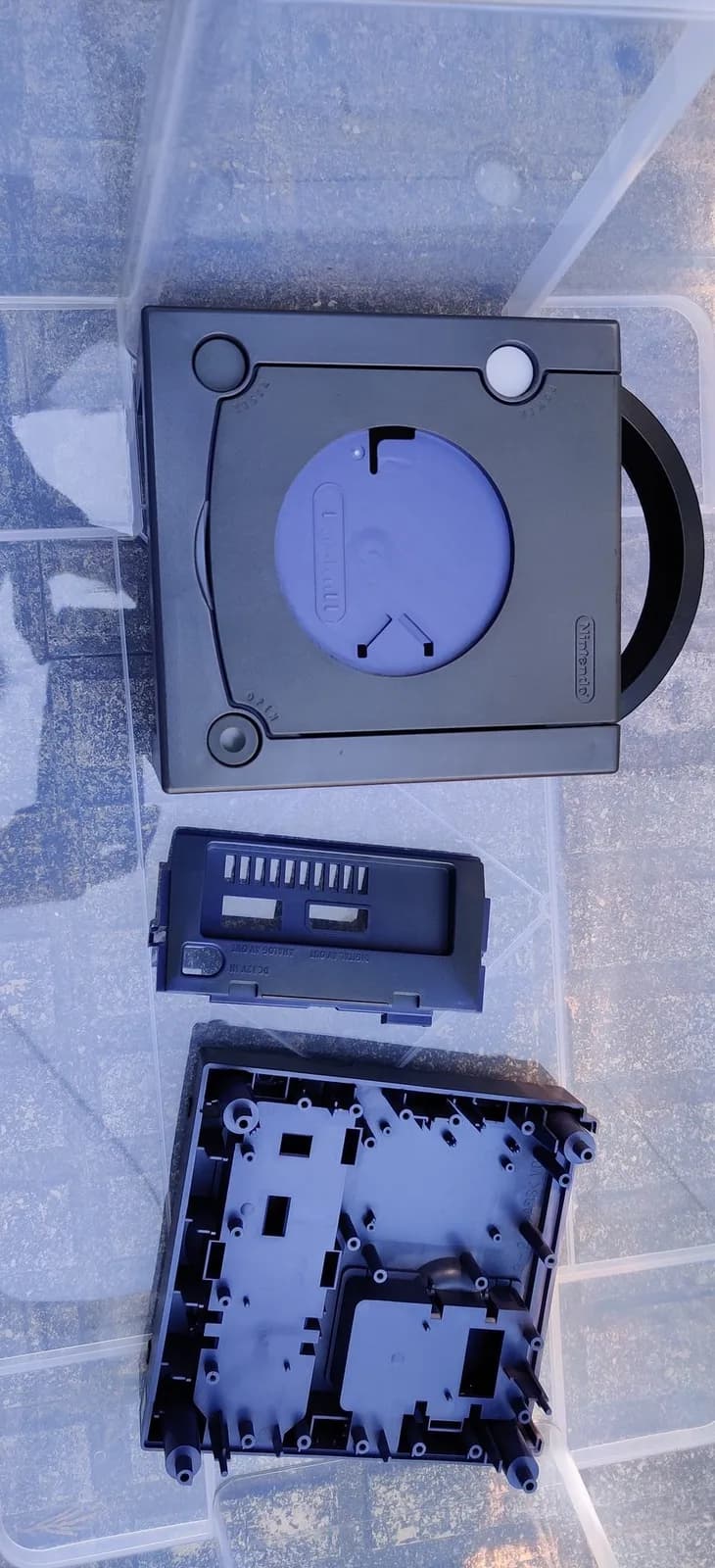 Disassembled indigo GameCube shell in a clear container before the retrobrite, no peroxide added yet: the top cover and the bottom housing.