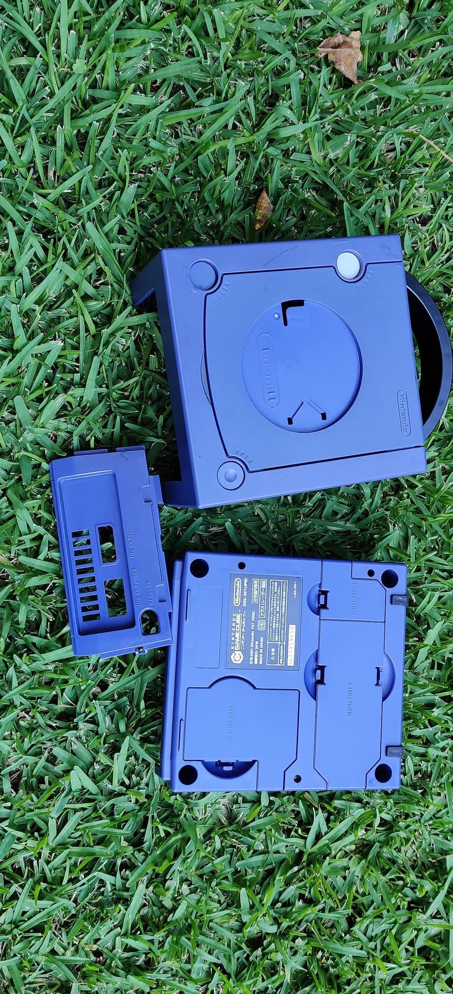 Disassembled Sega Saturn Model 2 plastic casing parts laid on grass showing retrobrite treatment progress, blue plastic shell components.
