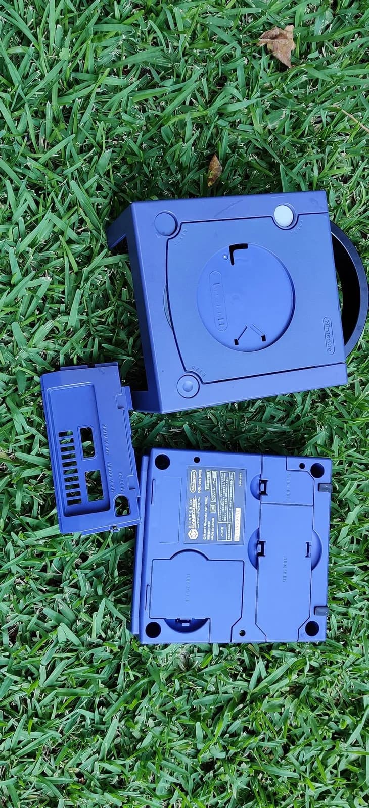 Disassembled indigo GameCube shell parts on grass after the retrobrite, showing how much the colour improved.