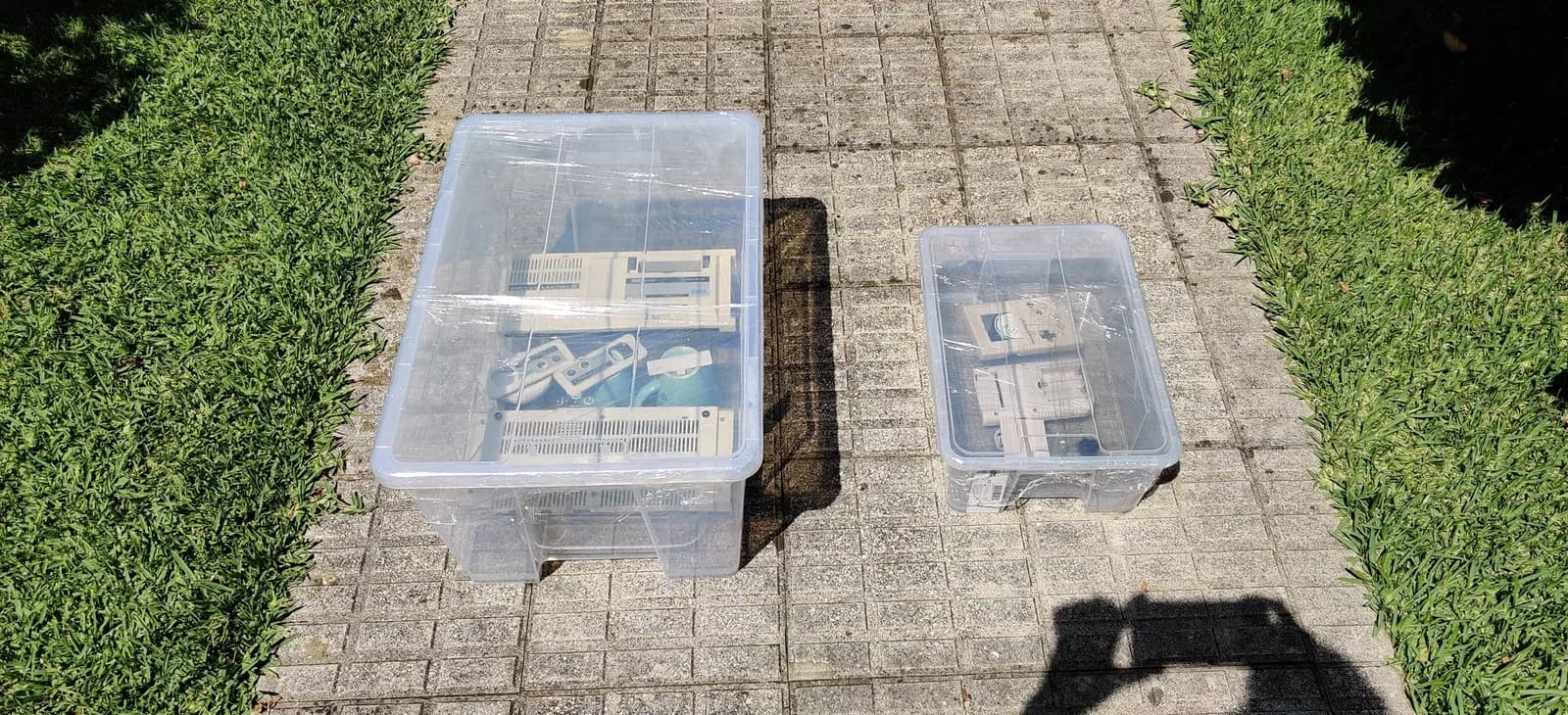 Two clear tubs out in the sun on brick paving during the retrobrite: the Sega Mark III shell halves and its Joypad controller shells along with the Game Boy DMG shells.