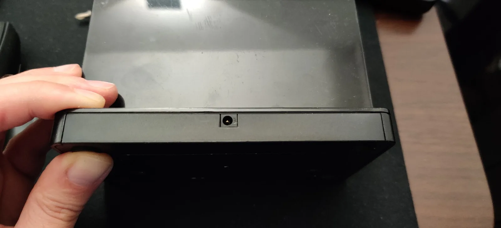 Logitech DiNovo Edge charging dock held in hand, showing replaced barrel jack connector on bottom edge.